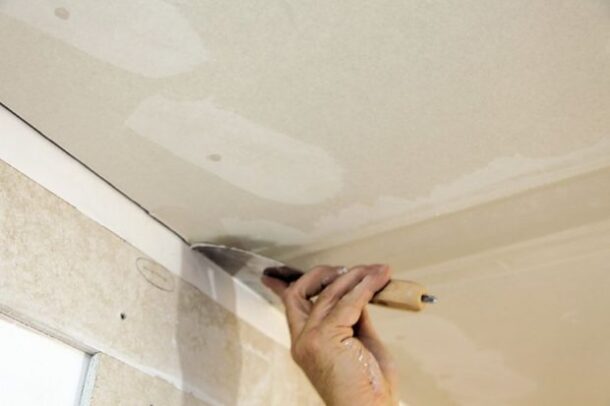 Процесс нанесения шпатлёвки на потолок с помощью шпателя для заделки трещин